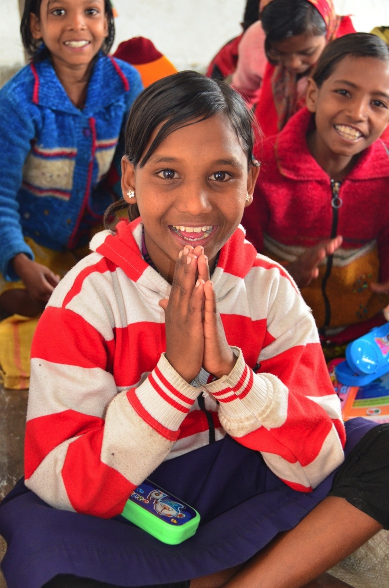 A smiling village school student greeting visitors with folded hands