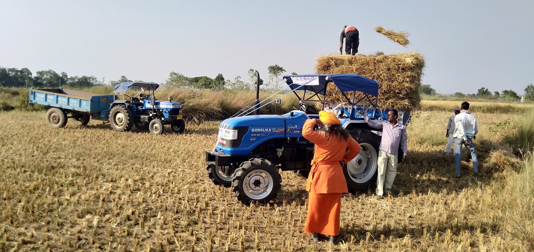 Farm workers gathering the harvest beside a tractor and trailer